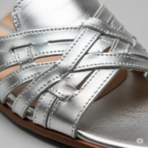 Close-up view of the metallic silver leather texture of flat sandals, highlighting the quality craftsmanship.